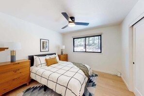 Un dormitorio con cama, mesitas de noche, ventilador de techo, ventana y puerta.