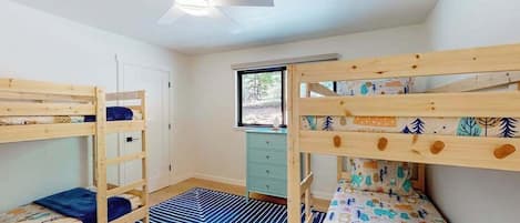 Una habitación con dos literas, un escritorio, una silla y una ventana con vistas a árboles.