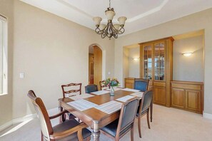 Uma sala de jantar com uma mesa de madeira, cadeiras, um candelabro e um aparador com portas de vidro.