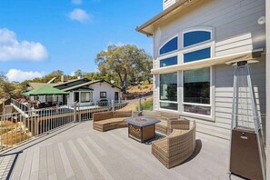 Um terraço com mobiliário de exterior, uma área coberta e vista para uma casa com grandes janelas.