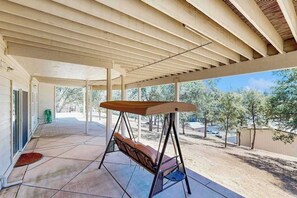A covered patio area with a swing chair, a door leading outside, and a view of trees and a fence. - Hemlock Hacienda - Pine Mountain Lake (Groveland)