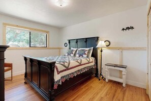 Un dormitorio con una cama de madera oscura, una mesita de noche, una lámpara y una ventana con vista a árboles.