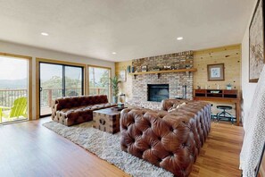 A spacious living room with a fireplace, leather sofas, and a balcony with a yellow chair. - Walling Mountain Retreat - Pine Mountain Lake (Groveland)