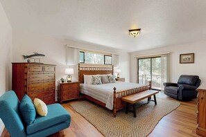 Ein Schlafzimmer mit Bett, Nachttischen, einer Bank, einem Sessel, einem Kleiderschrank und einem Fenster.