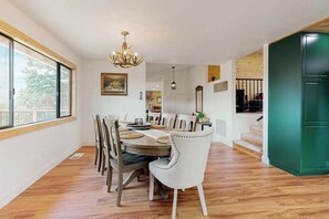 Un comedor con una mesa de madera, sillas blancas y una araña.
