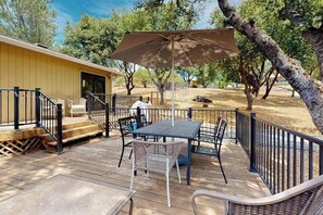 An outdoor deck with a table and chairs, a covered umbrella, and a building in the background. - Walling Mountain Retreat - Pine Mountain Lake (Groveland)