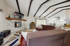A modern living room with a fireplace, a sofa, a television, and a dining area with a chandelier. - Pleasant Pines Retreat - Pine Mountain Lake (Groveland)
