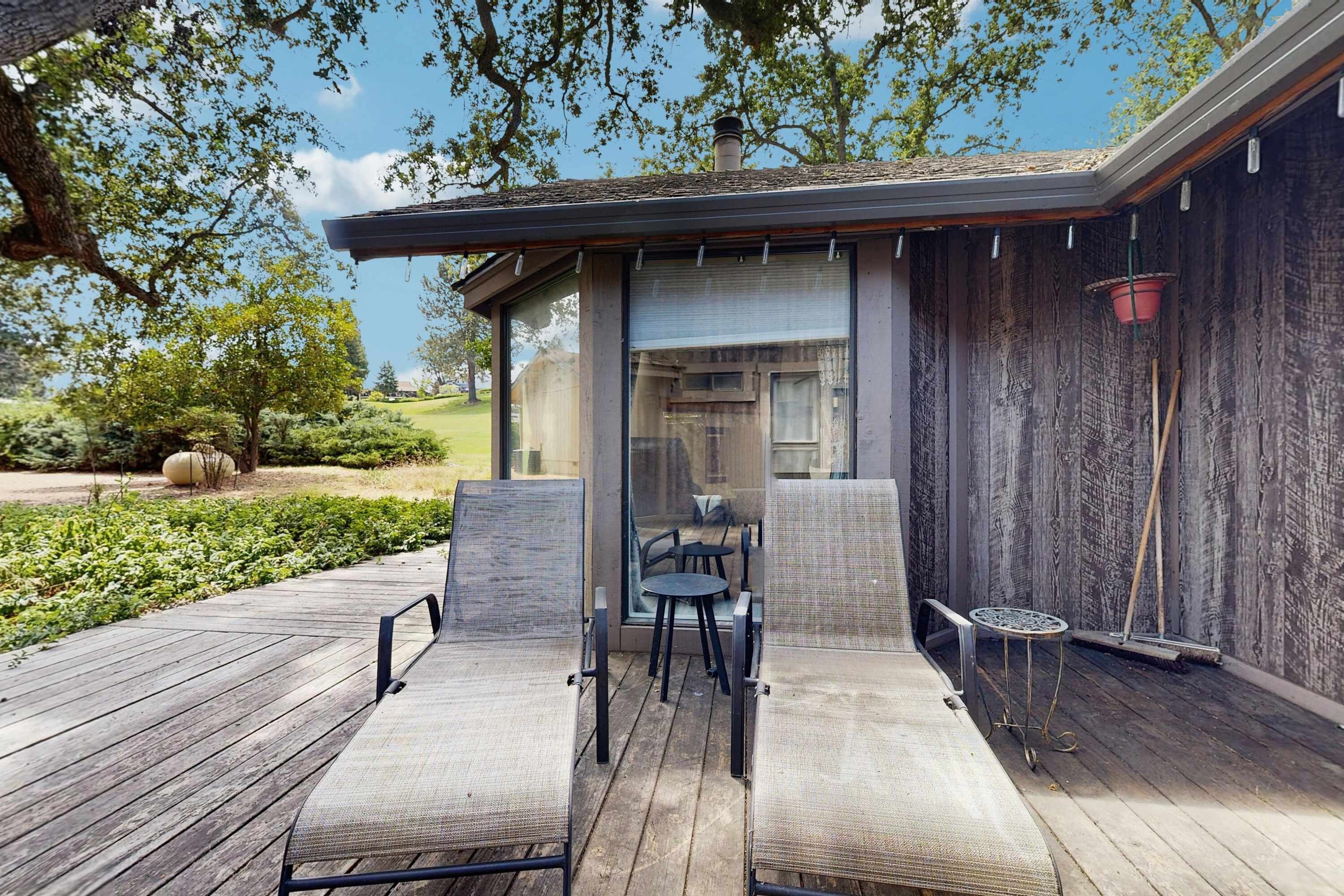 A covered outdoor seating area with two lounge chairs and a small table, overlooking a landscaped garden.