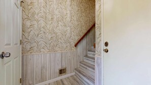 A hallway with a patterned wallpaper, wooden paneling, a wooden staircase, and a door with a round doorknob. - Pleasant Pines Retreat - Pine Mountain Lake (Groveland)