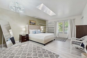 Une chambre à coucher comprenant un lit, des tables de chevet, un miroir, une fenêtre avec des rideaux et un luminaire suspendu.