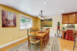 A dining area with a wooden table and chairs, a rug, and artwork on the walls. - Cypress Lodge - Blue Lake Springs (Arnold)