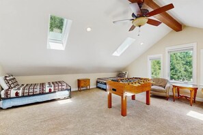 A cozy loft bedroom with a futon, a foosball table, a ceiling fan, and large windows offering a view of greenery. - Cypress Lodge - Blue Lake Springs (Arnold)