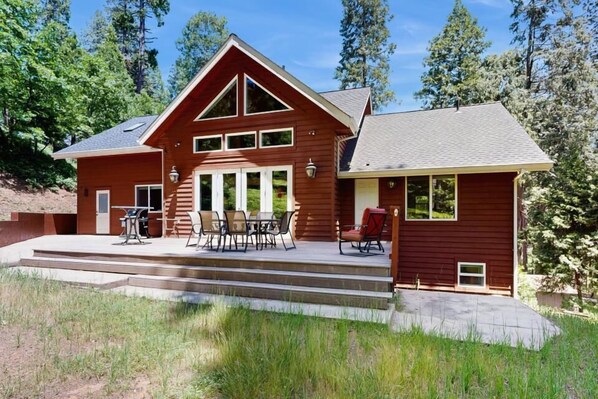 Une maison en bois à deux étages, dotée d’un patio couvert et d’un espace extérieur aménagé pour s’asseoir.