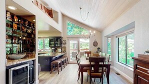 A spacious kitchen with a bar area, wooden flooring, and large windows offering views of the outdoors. - Windwood Inn - Ockenden Ranch (Shaver Lake)