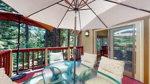 A glass-top table with chairs, a red railing, and a large umbrella providing shade. - Windwood Inn - Ockenden Ranch (Shaver Lake)