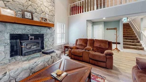 A stone fireplace, a brown leather sofa, and a staircase leading to a second floor. - Windwood Inn - Ockenden Ranch (Shaver Lake)