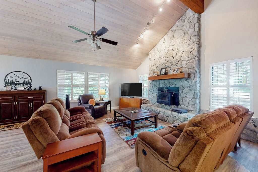 Una sala de estar con chimenea de piedra, ventilador de techo y televisor de pantalla plana.