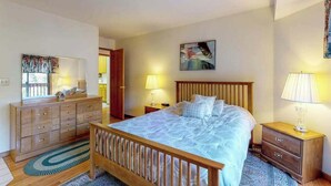 A bedroom with a wooden bed, a dresser, a nightstand, and a painting on the wall. - Lake Lodge Retreat - Pine Mountain Lake (Groveland)