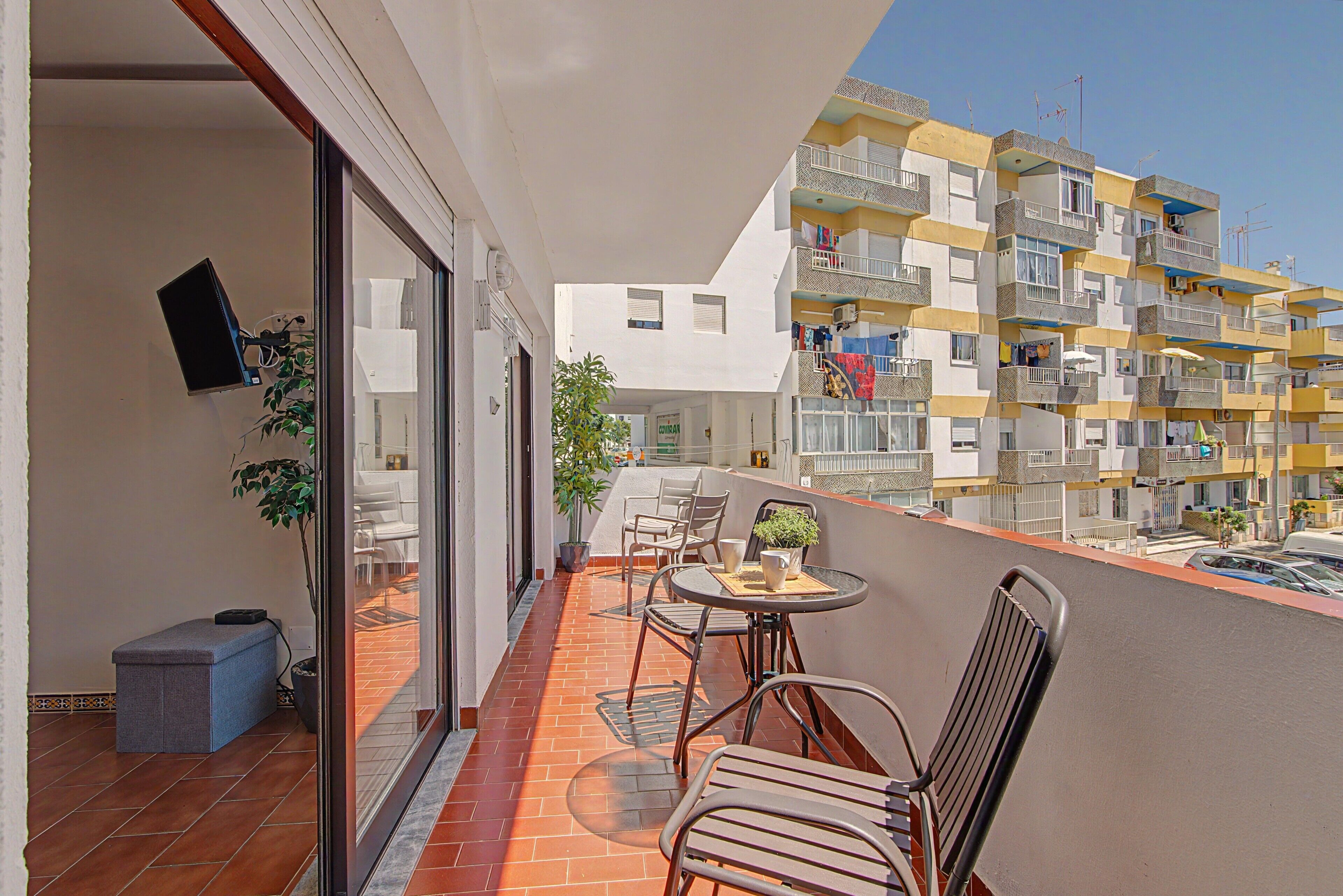 A balcony with a table and chairs, a potted plant, and a view of a multi-story building with balconies.