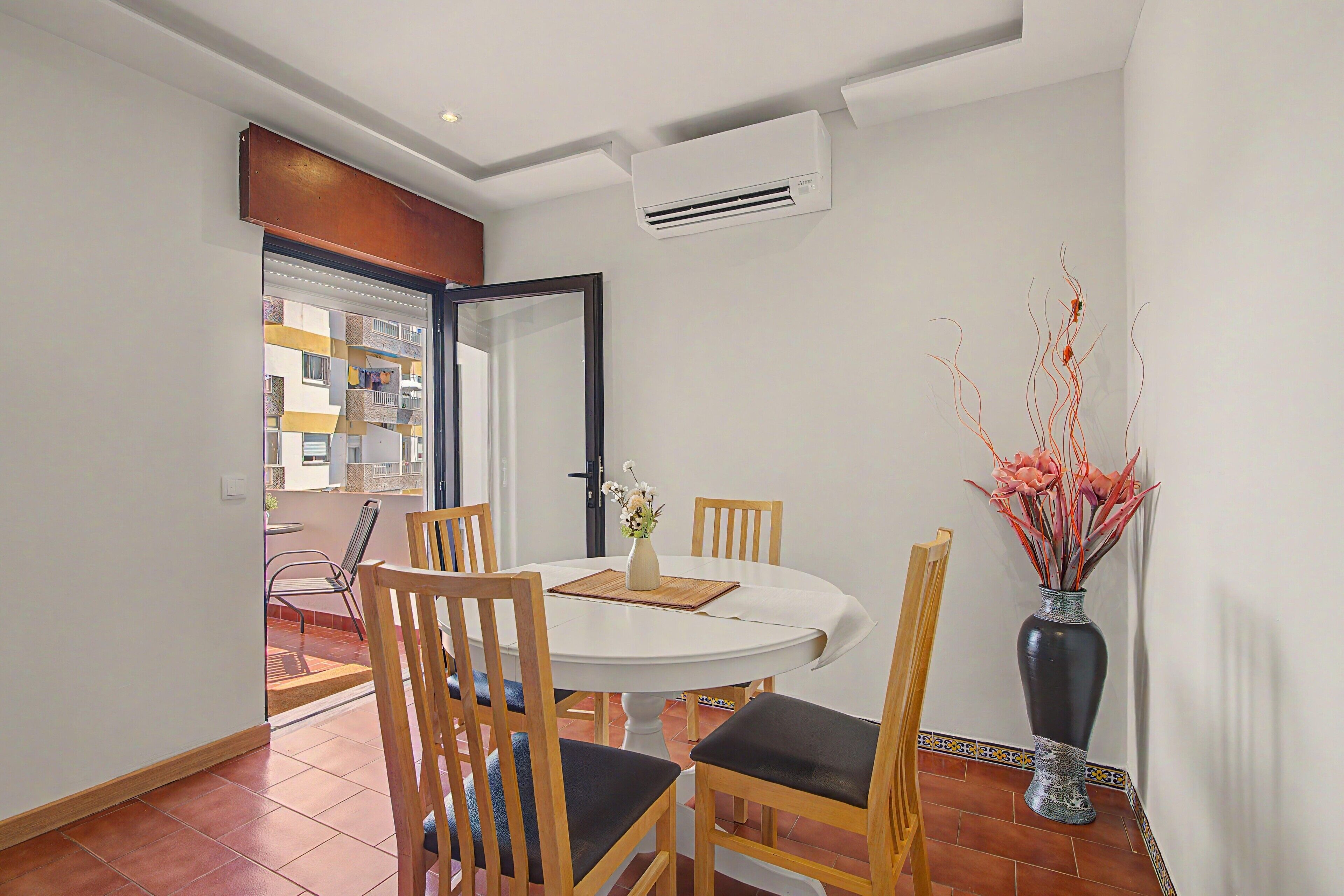 A dining area with a round table, four chairs, a vase with flowers, and a potted plant.