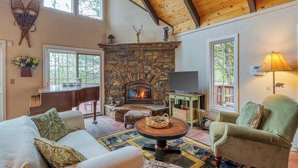 A cozy living room with a stone fireplace, comfortable seating, and large windows. - Forest Bear's Hideout - Blue Lake Springs (Arnold)