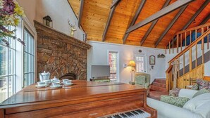 A grand piano in a well-lit room with a stone fireplace, a staircase, and a cozy seating area. - Forest Bear's Hideout - Blue Lake Springs (Arnold)