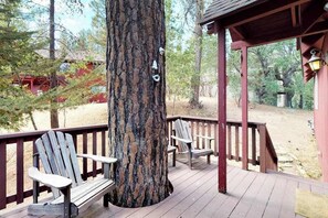 Een houten terras met Adirondack stoelen en een grote boomstam.
