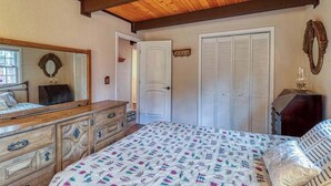 A bedroom with a wooden ceiling, a bed with patterned bedding, a dresser, a mirror, and a closet. - Forest Bear's Hideout - Blue Lake Springs (Arnold)