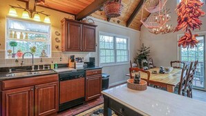 A kitchen with wooden cabinets, a dishwasher, a sink, and a dining area with a table and chairs. - Forest Bear's Hideout - Blue Lake Springs (Arnold)