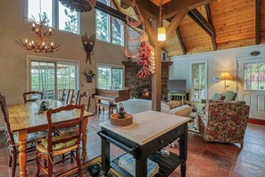 A spacious living room with a fireplace, wooden beams, and a dining area with chairs and a table. - Forest Bear's Hideout - Blue Lake Springs (Arnold)