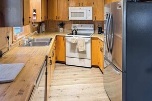 A compact kitchen with wooden cabinets, a stainless steel refrigerator, a microwave, and a stove. - Rustic Retreat - Pine Mountain Lake (Groveland)