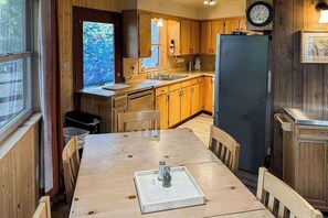 A compact kitchen with wooden cabinets, a refrigerator, and a window with a colorful view. - Rustic Retreat - Pine Mountain Lake (Groveland)