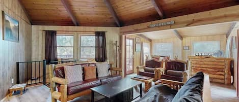 A log cabin interior with a wooden ceiling, a sofa, a table, and a fireplace.