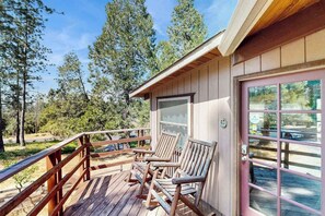 A wooden deck with two rocking chairs, a wooden railing, and a building with a glass door. - Rustic Retreat - Pine Mountain Lake (Groveland)