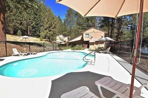 A swimming pool with lounge chairs and umbrellas, surrounded by a fence and trees.