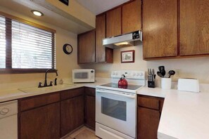 A compact kitchen with wooden cabinets, a white stove, a microwave, and a toaster. - Blue Jay Condominium - Huntington Lake (Lakeshore)