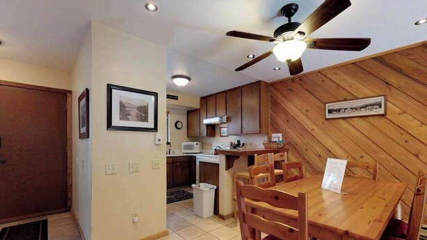 A dining area with a wooden table and chairs, a ceiling fan, and a kitchen in the background. - Blue Jay Condominium - Huntington Lake (Lakeshore)