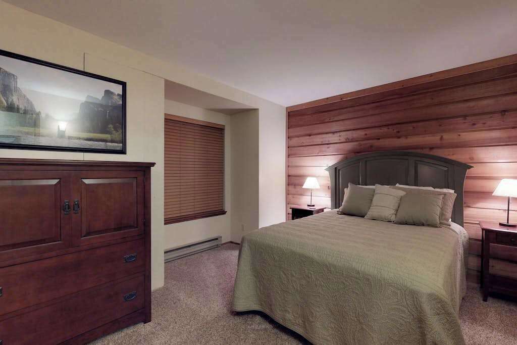Une chambre à coucher avec un lit, une commode, un tableau et des lambris en bois sur les murs.