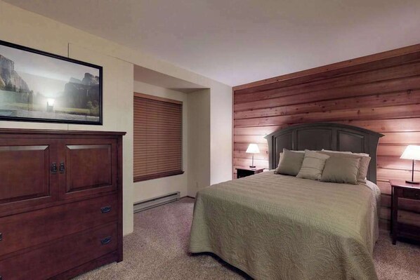 A bedroom with a bed, a dresser, a painting, and wooden paneling on the walls.