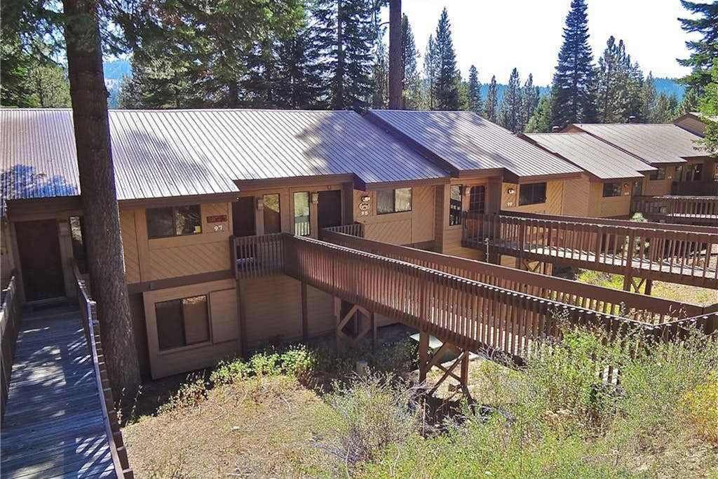 Une rangée de cabanes reliées par une terrasse en bois, le tout entouré d’arbres.