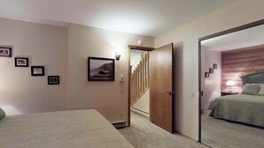 A bedroom with a bed, a door leading to a staircase, and a wall with framed pictures. - Blue Jay Condominium - Huntington Lake (Lakeshore)