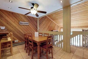 A dining area with a wooden table and chairs, a ceiling fan, and a view of the outside.