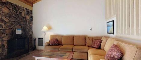 A living room with a stone fireplace, a wooden ceiling, a beige sofa, and a coffee table.