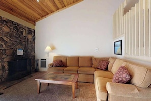 A living room with a stone fireplace, a wooden ceiling, a beige sofa, and a coffee table.