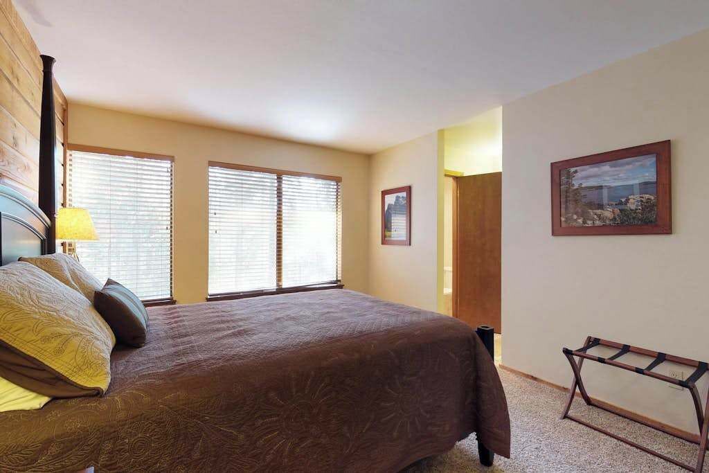 Un dormitorio con una cama, dos ventanas, una puerta y un cuadro en la pared.