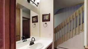 A bathroom with a white sink, a mirror, and a wooden staircase in the background. - Blue Jay Condominium - Huntington Lake (Lakeshore)