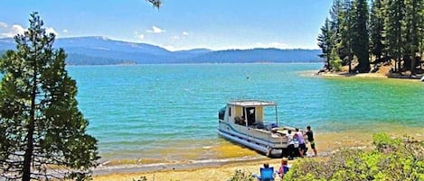 Um lago com um barco atracado perto da margem, rodeado por árvores e montanhas ao fundo.