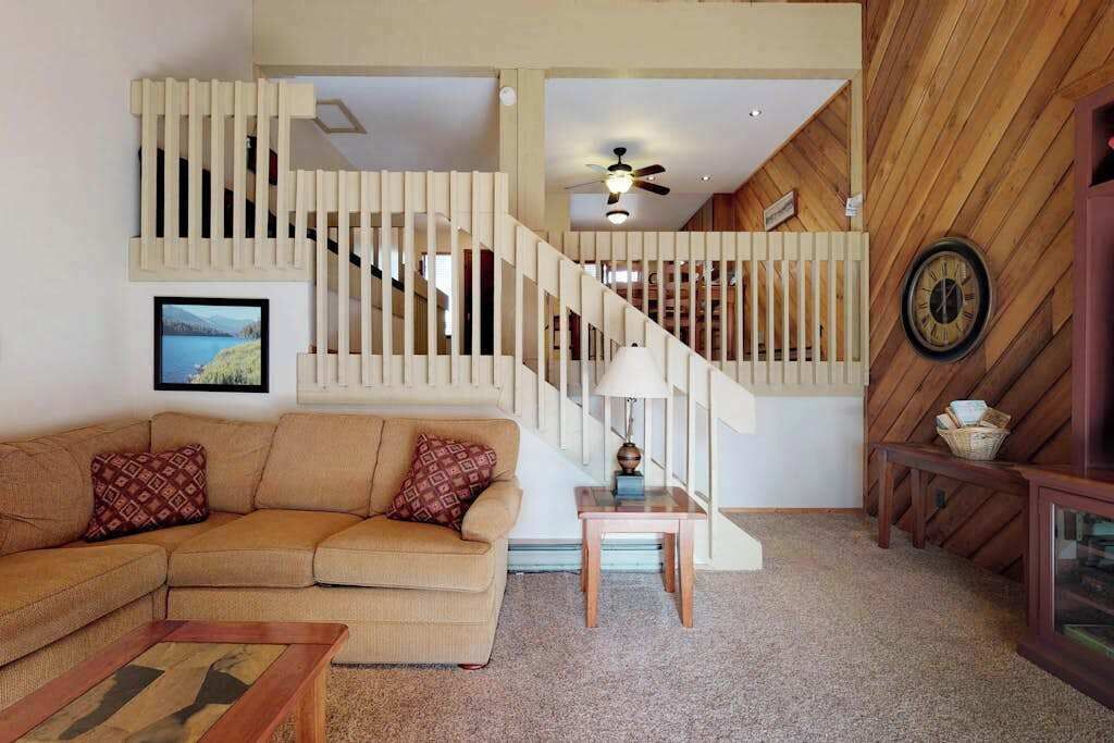 A living room with a beige sectional sofa, a small wooden coffee table, a lamp, and a staircase with wooden railings.