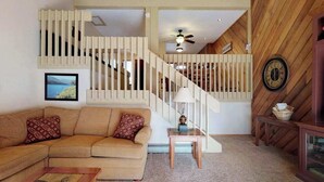A living room with a beige sectional sofa, a small wooden coffee table, a lamp, and a staircase with wooden railings. - Blue Jay Condominium - Huntington Lake (Lakeshore)