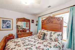 A bedroom with a wooden headboard, floral bedding, a bedside table with a lamp, and a window with curtains. - Under The Stars - Shaver Lake (Shaver Lake)